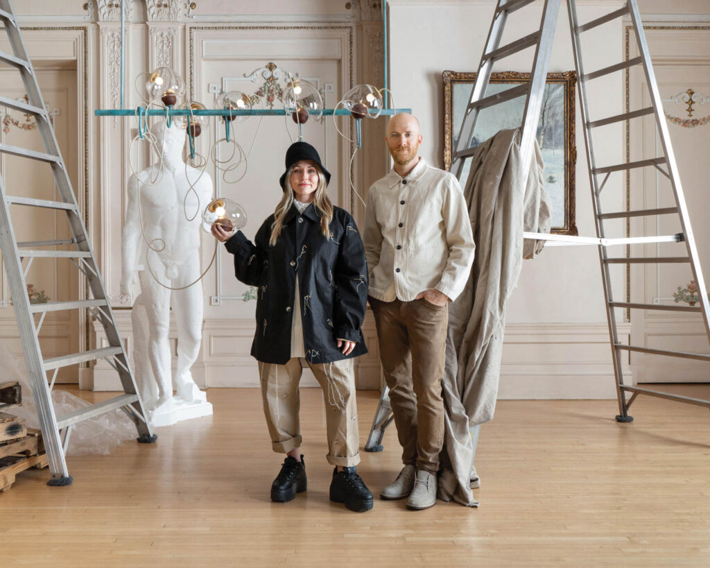 two people standing in room with lighting, ladders and statue