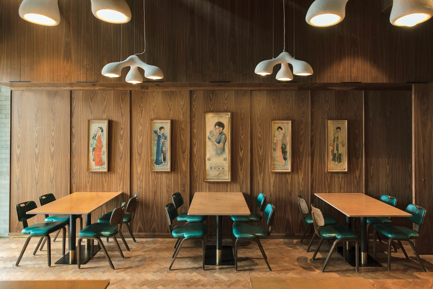 dining area of a restaurant with wooden paneled walls, tables with teal chairs and pictures of Chinese paintings on the wall